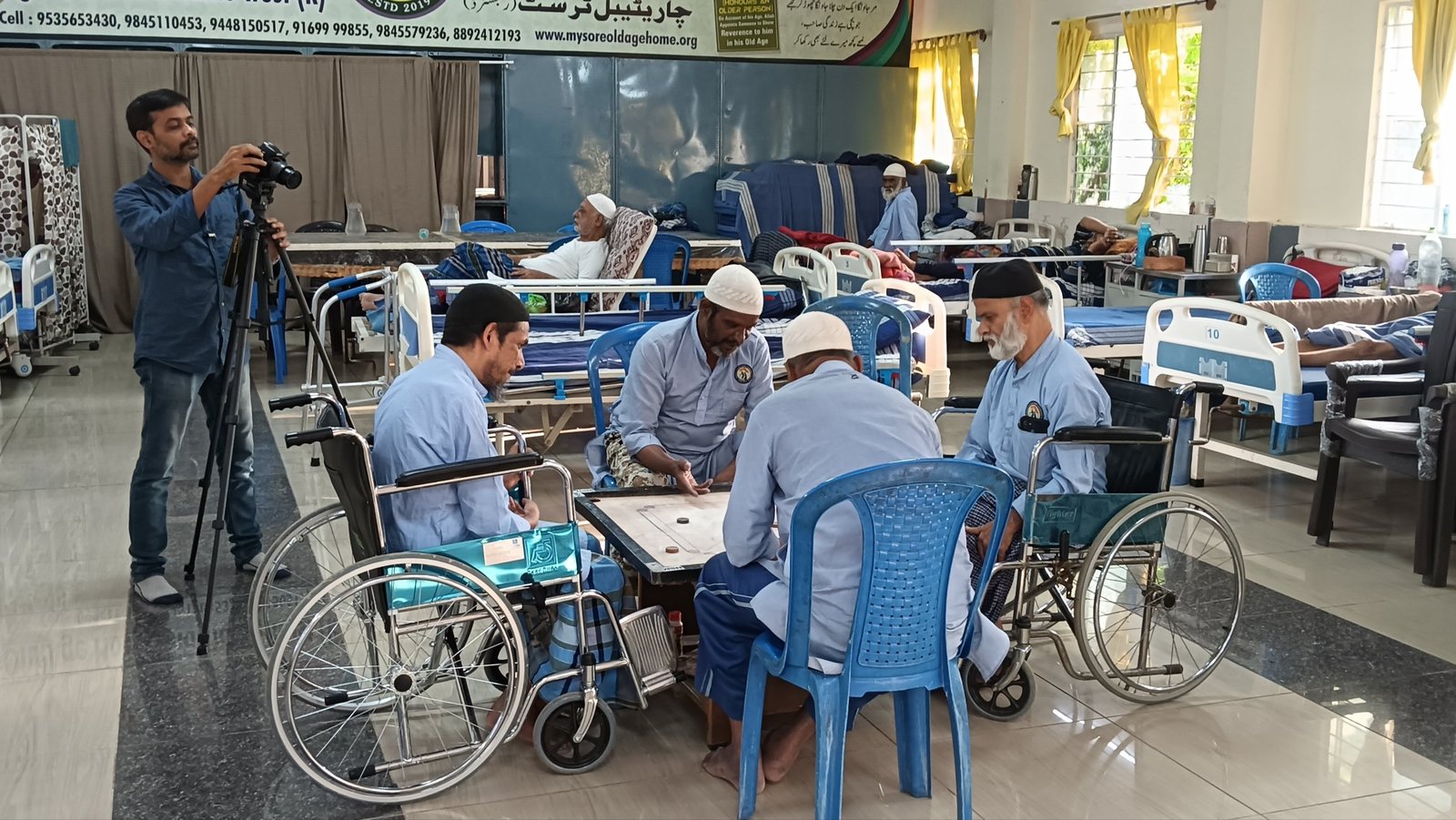 Four residents, two of them in wheelchairs, playing a game of carrom together in the hall